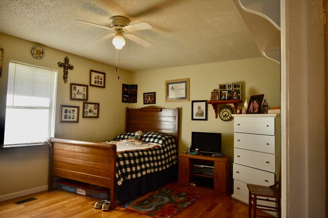 bedroom with ceiling fan, hardwood / wood-style floors, and a textured ceiling