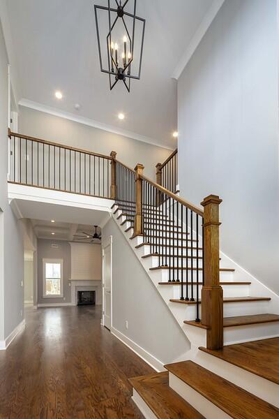 staircase with ornamental molding, wood-type flooring, ceiling fan with notable chandelier, and a high ceiling