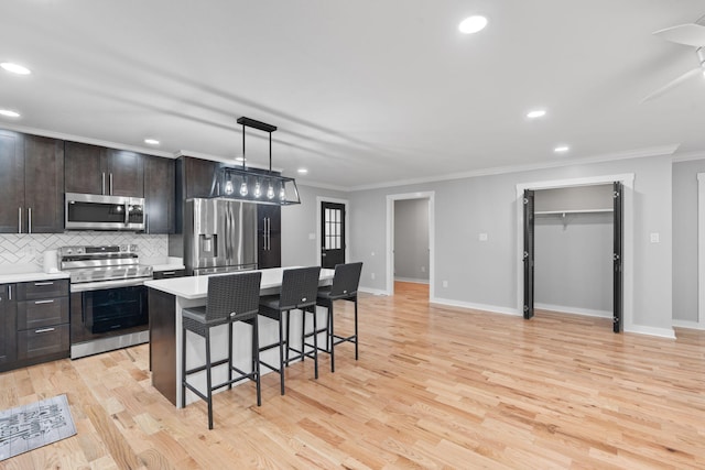 kitchen featuring appliances with stainless steel finishes, a breakfast bar area, light countertops, tasteful backsplash, and ornamental molding