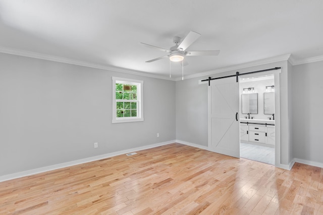 unfurnished bedroom featuring crown molding, a barn door, a sink, light wood-style floors, and baseboards