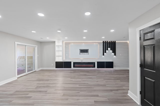 unfurnished living room with baseboards, recessed lighting, a glass covered fireplace, and wood finished floors