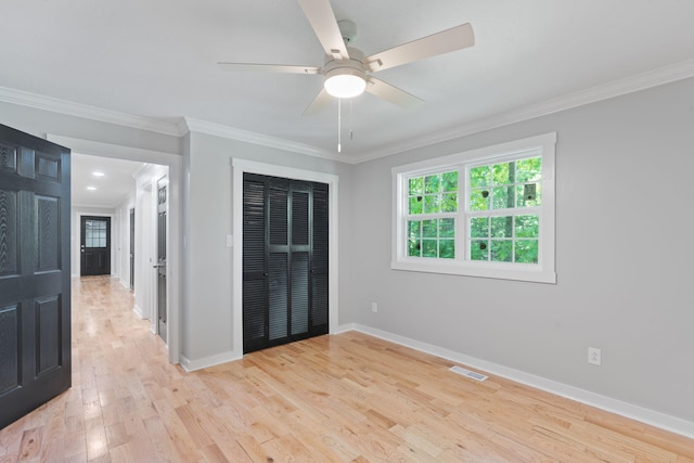 unfurnished bedroom with crown molding, light wood finished floors, baseboards, visible vents, and a closet