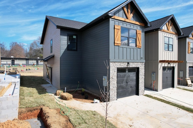 view of property exterior featuring stone siding, roof with shingles, board and batten siding, concrete driveway, and an attached garage