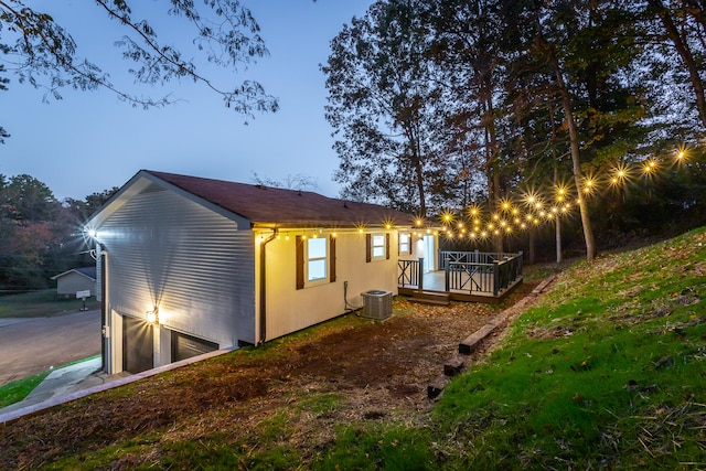 property exterior at dusk featuring a wooden deck, cooling unit, and a garage