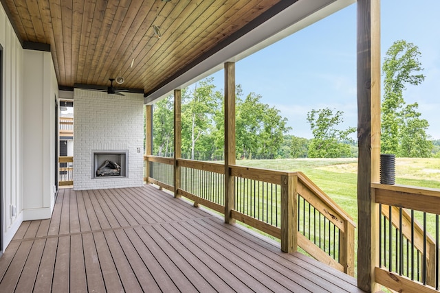 wooden deck with a lawn, an outdoor brick fireplace, and ceiling fan