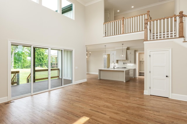 unfurnished living room featuring crown molding, sink, light hardwood / wood-style floors, and a high ceiling