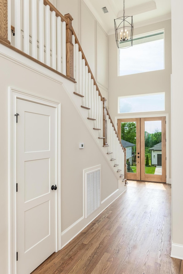 foyer entrance featuring hardwood / wood-style floors, a towering ceiling, french doors, and a healthy amount of sunlight