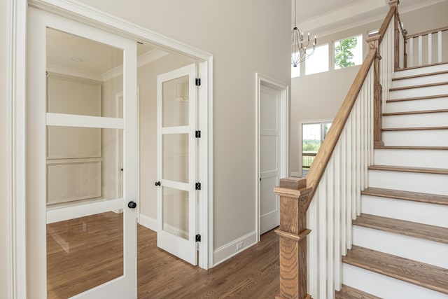 stairway with a wealth of natural light, crown molding, wood-type flooring, and a notable chandelier