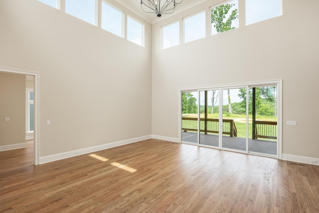 unfurnished living room featuring hardwood / wood-style floors, a towering ceiling, a healthy amount of sunlight, and a notable chandelier