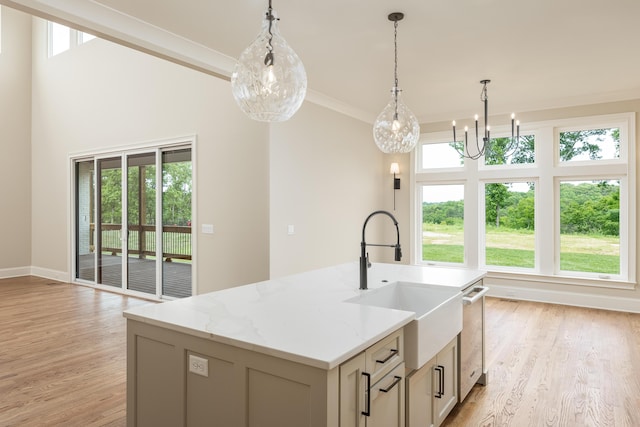 kitchen featuring light stone counters, crown molding, a center island with sink, light hardwood / wood-style floors, and hanging light fixtures