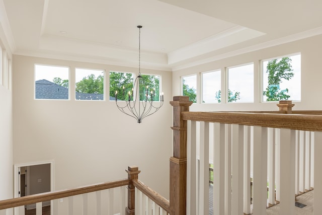 staircase with ornamental molding, a raised ceiling, plenty of natural light, and a notable chandelier