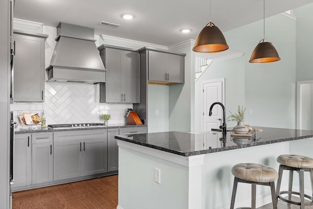 kitchen featuring premium range hood, an island with sink, pendant lighting, and stainless steel gas cooktop