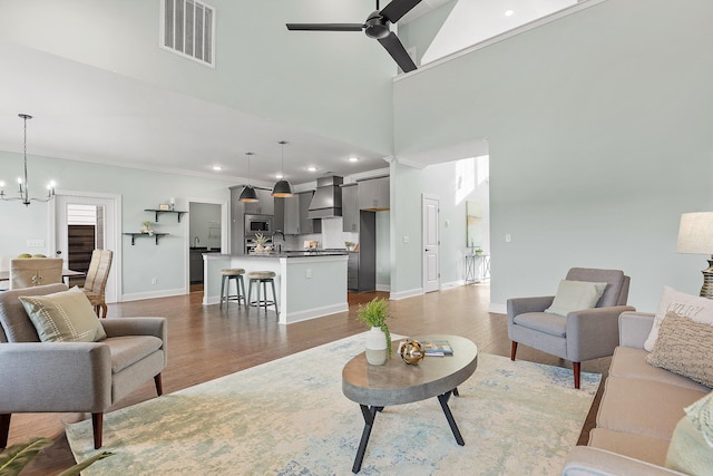 living room with sink, ceiling fan with notable chandelier, a high ceiling, and hardwood / wood-style flooring