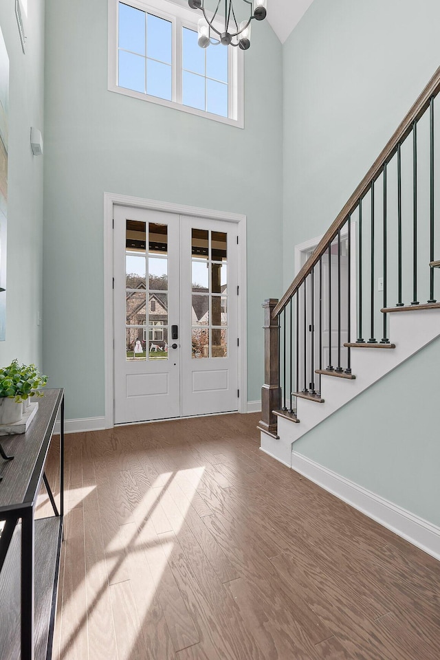 foyer featuring french doors, a towering ceiling, hardwood / wood-style floors, and a notable chandelier