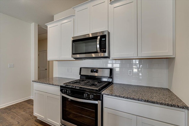 kitchen with backsplash, stainless steel appliances, dark stone countertops, dark hardwood / wood-style floors, and white cabinetry