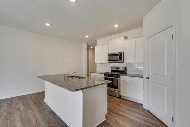 kitchen with white cabinetry, sink, stainless steel appliances, dark hardwood / wood-style floors, and an island with sink