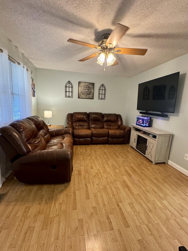living area with baseboards, a textured ceiling, a ceiling fan, and light wood-style floors