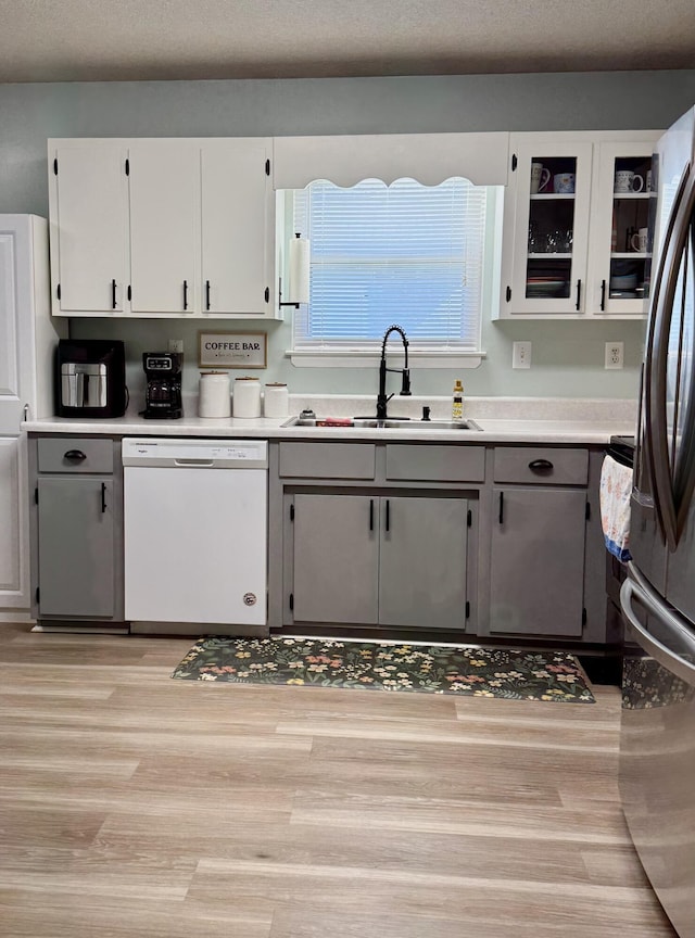 kitchen with white cabinetry, light countertops, white dishwasher, and a sink