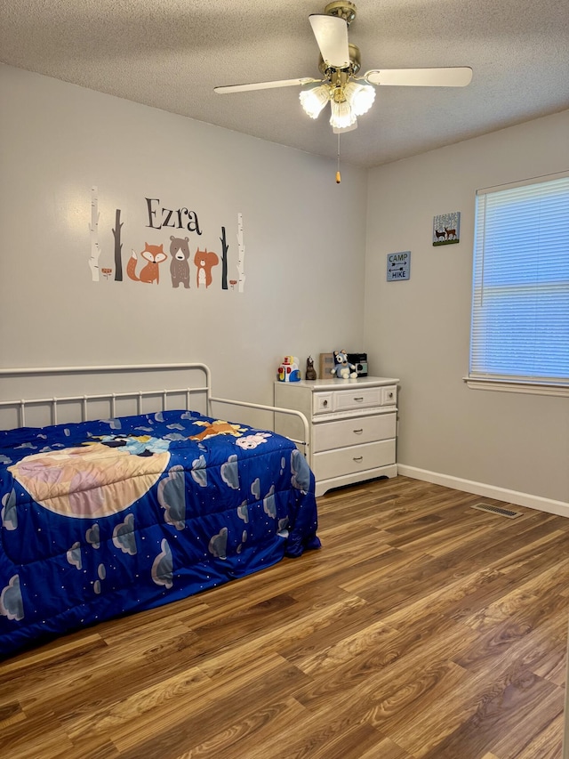 bedroom with wood finished floors, baseboards, visible vents, ceiling fan, and a textured ceiling