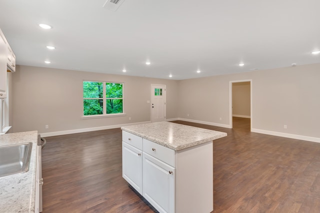 kitchen with dark hardwood / wood-style flooring, white cabinetry, a kitchen island, and light stone counters