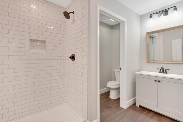 bathroom featuring a tile shower, vanity, hardwood / wood-style flooring, and toilet