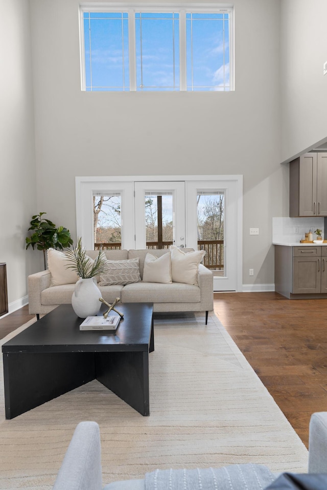 living room featuring a healthy amount of sunlight, light hardwood / wood-style flooring, french doors, and a towering ceiling
