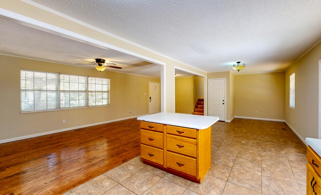 kitchen with a center island, crown molding, ceiling fan, light wood-type flooring, and a textured ceiling