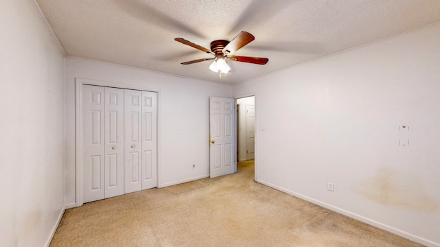 unfurnished bedroom with ceiling fan, a textured ceiling, light carpet, a closet, and ornamental molding