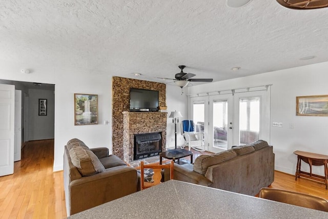 5027 Fanchers Mill Rd, Sparta, TN 38583 - living room featuring a textured ceiling, french doors, a ceiling fan, a stone fireplace, and light wood finished floors