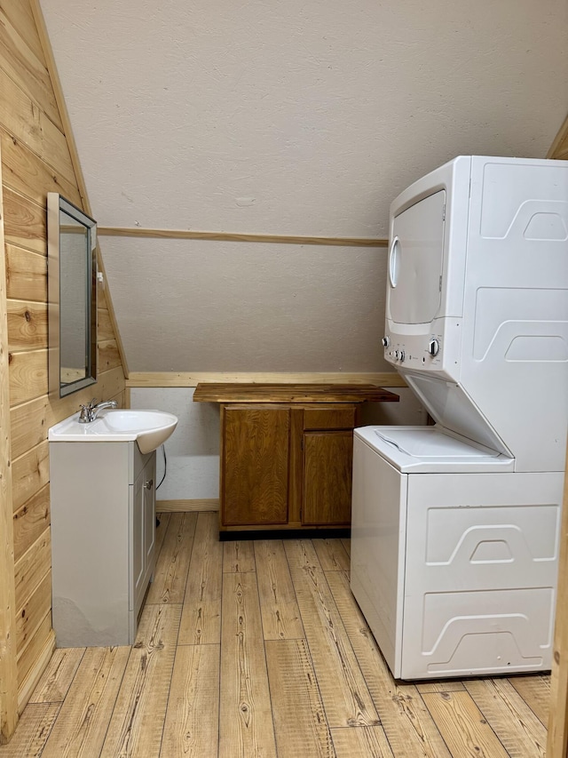 laundry area with wooden walls, light hardwood / wood-style flooring, stacked washer and clothes dryer, and sink