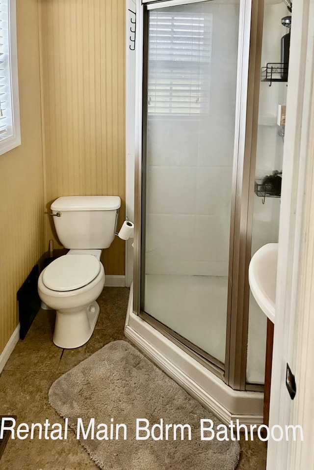 bathroom with tile patterned flooring, toilet, a shower with shower door, and a wealth of natural light
