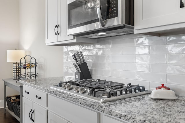 kitchen featuring light stone countertops, white cabinetry, backsplash, and appliances with stainless steel finishes