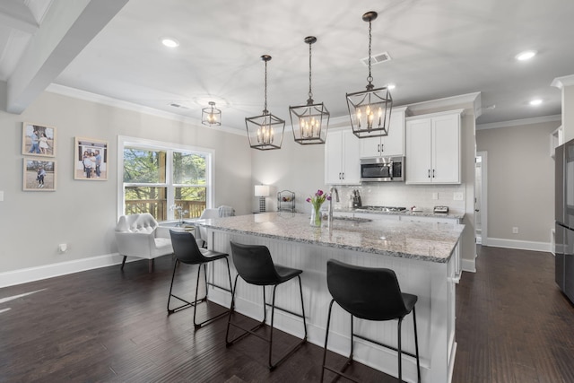 kitchen with white cabinetry, dark wood-type flooring, hanging light fixtures, stainless steel appliances, and an island with sink