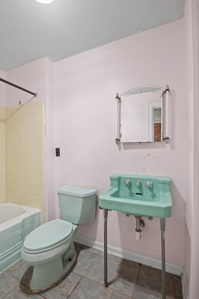 bathroom featuring shower / bathing tub combination, toilet, a sink, and baseboards