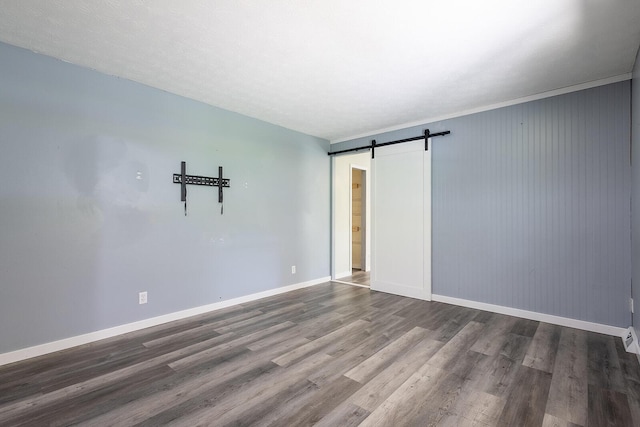 unfurnished room with wood finished floors, a barn door, and baseboards