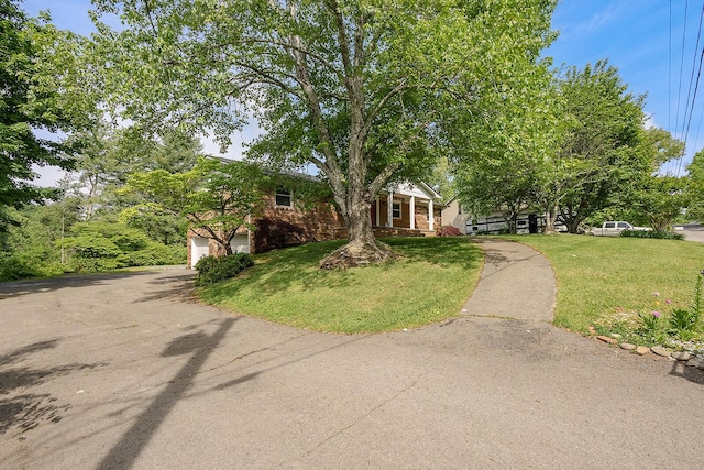obstructed view of property with a front yard, brick siding, a garage, and driveway