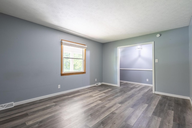 spare room with a textured ceiling, baseboards, visible vents, and dark wood finished floors