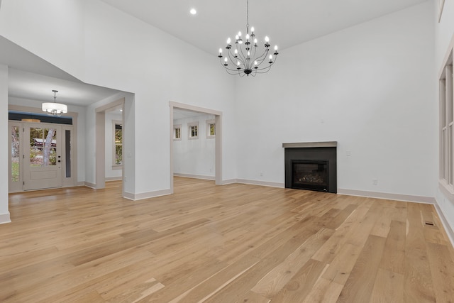 unfurnished living room with high vaulted ceiling, light hardwood / wood-style floors, and an inviting chandelier