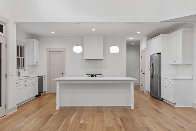 kitchen with custom exhaust hood, white cabinetry, hanging light fixtures, and light hardwood / wood-style flooring