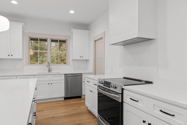 kitchen featuring white cabinets, light hardwood / wood-style floors, premium range hood, and appliances with stainless steel finishes