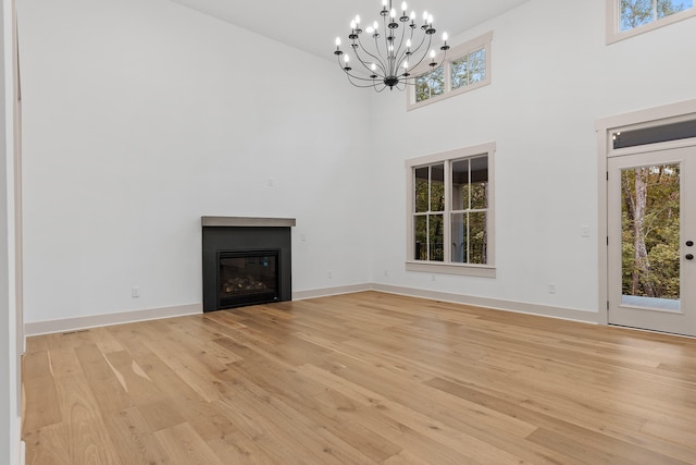 unfurnished living room featuring a towering ceiling, an inviting chandelier, and light hardwood / wood-style flooring