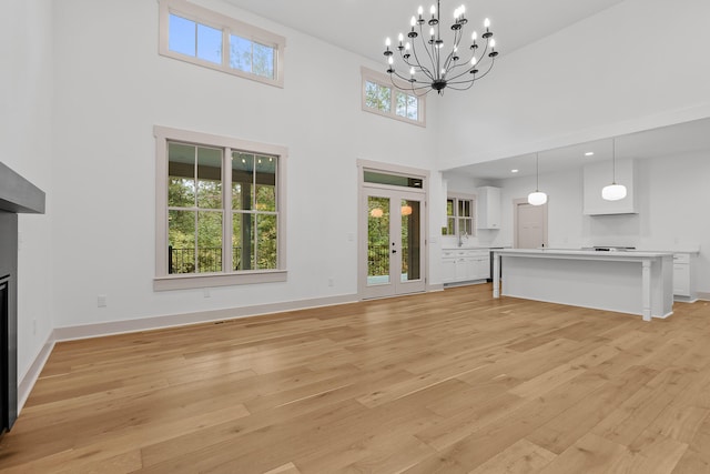 unfurnished living room with a chandelier, french doors, a high ceiling, and light hardwood / wood-style flooring