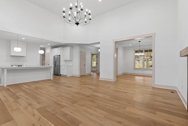 unfurnished living room featuring a high ceiling, light wood-type flooring, and an inviting chandelier