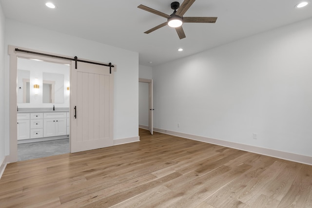 unfurnished bedroom with ensuite bath, ceiling fan, sink, a barn door, and light wood-type flooring