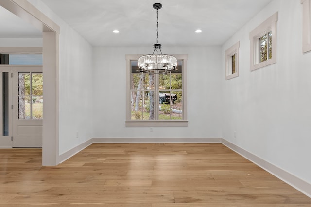 unfurnished dining area with plenty of natural light, an inviting chandelier, and light hardwood / wood-style flooring