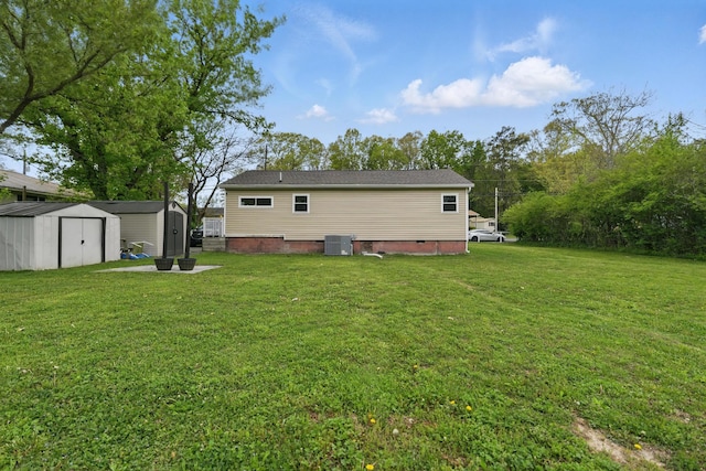 back of house with a lawn, crawl space, a storage unit, central air condition unit, and an outbuilding