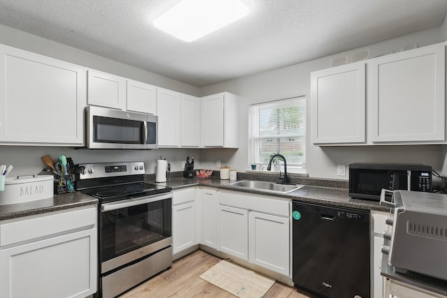 kitchen with light wood-style floors, white cabinets, black appliances, a sink, and dark countertops