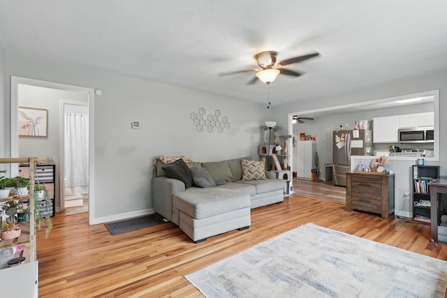 living room featuring light wood-style flooring, ceiling fan, and baseboards