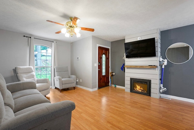 living room with ceiling fan, a large fireplace, light hardwood / wood-style floors, and a textured ceiling