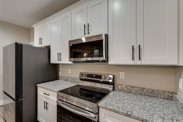 kitchen with light stone countertops, stainless steel appliances, hardwood / wood-style floors, and white cabinets